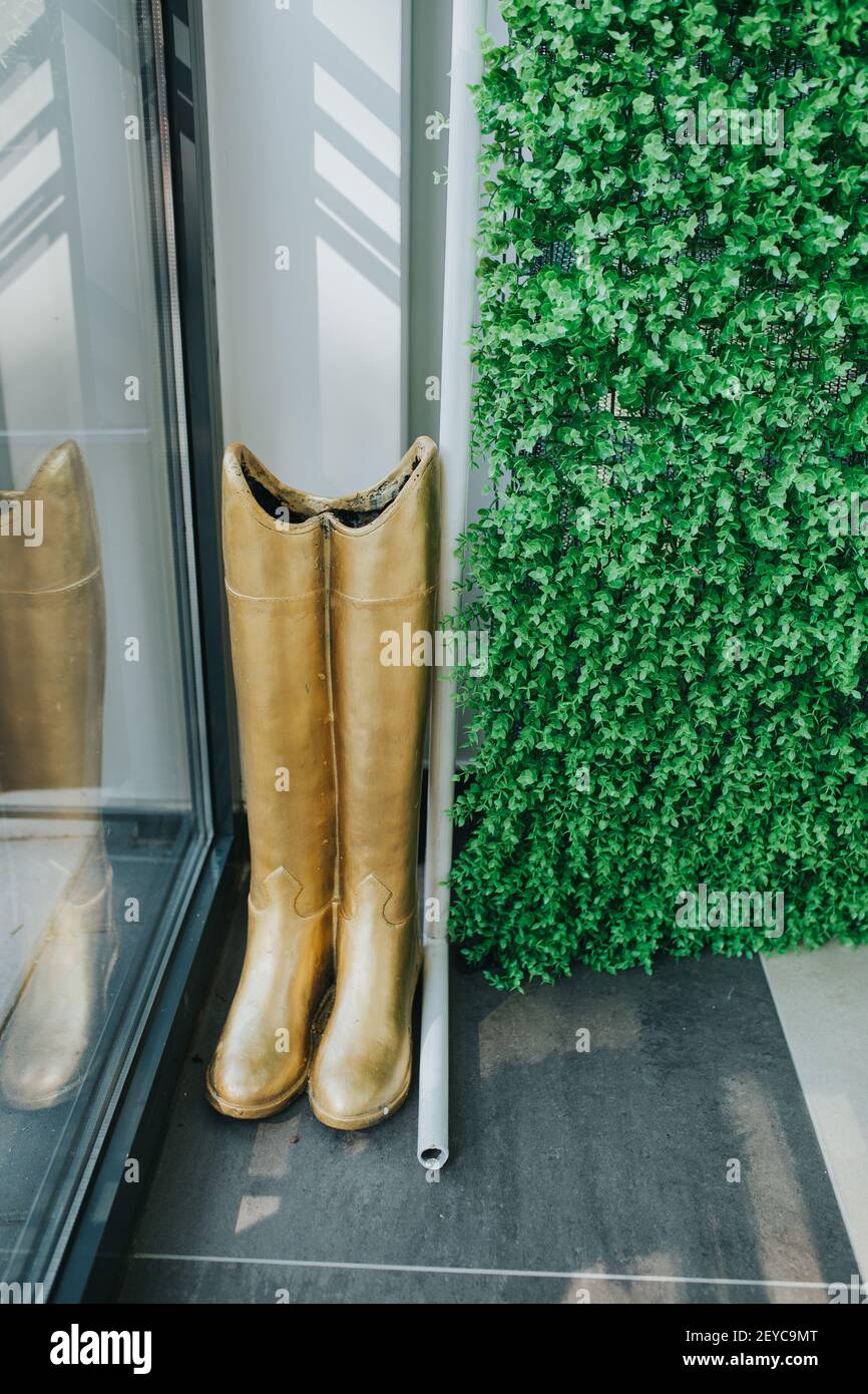Un'immagine verticale degli stivali dorati visualizzati accanto a. vetrata  del negozio Foto stock - Alamy