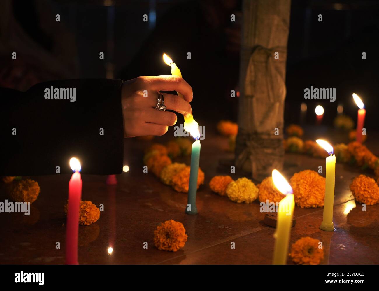 Un closeup di messa a fuoco selettiva di una mano che illumina un colorato candela intorno ad un palo con fiori Foto Stock