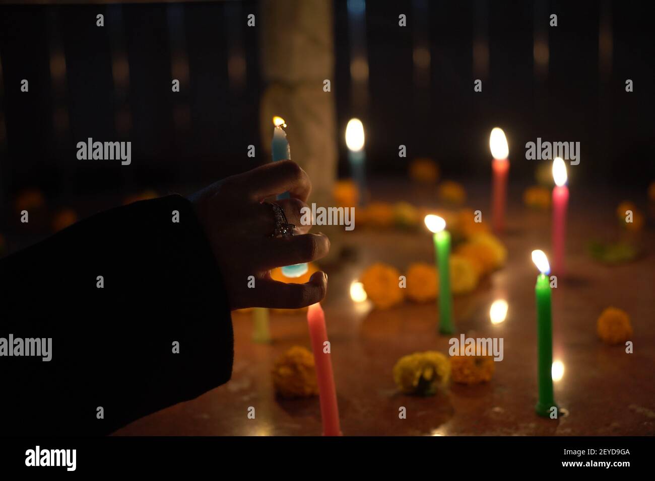 Un closeup di messa a fuoco selettiva di una mano che illumina un colorato candela intorno ad un palo con fiori Foto Stock