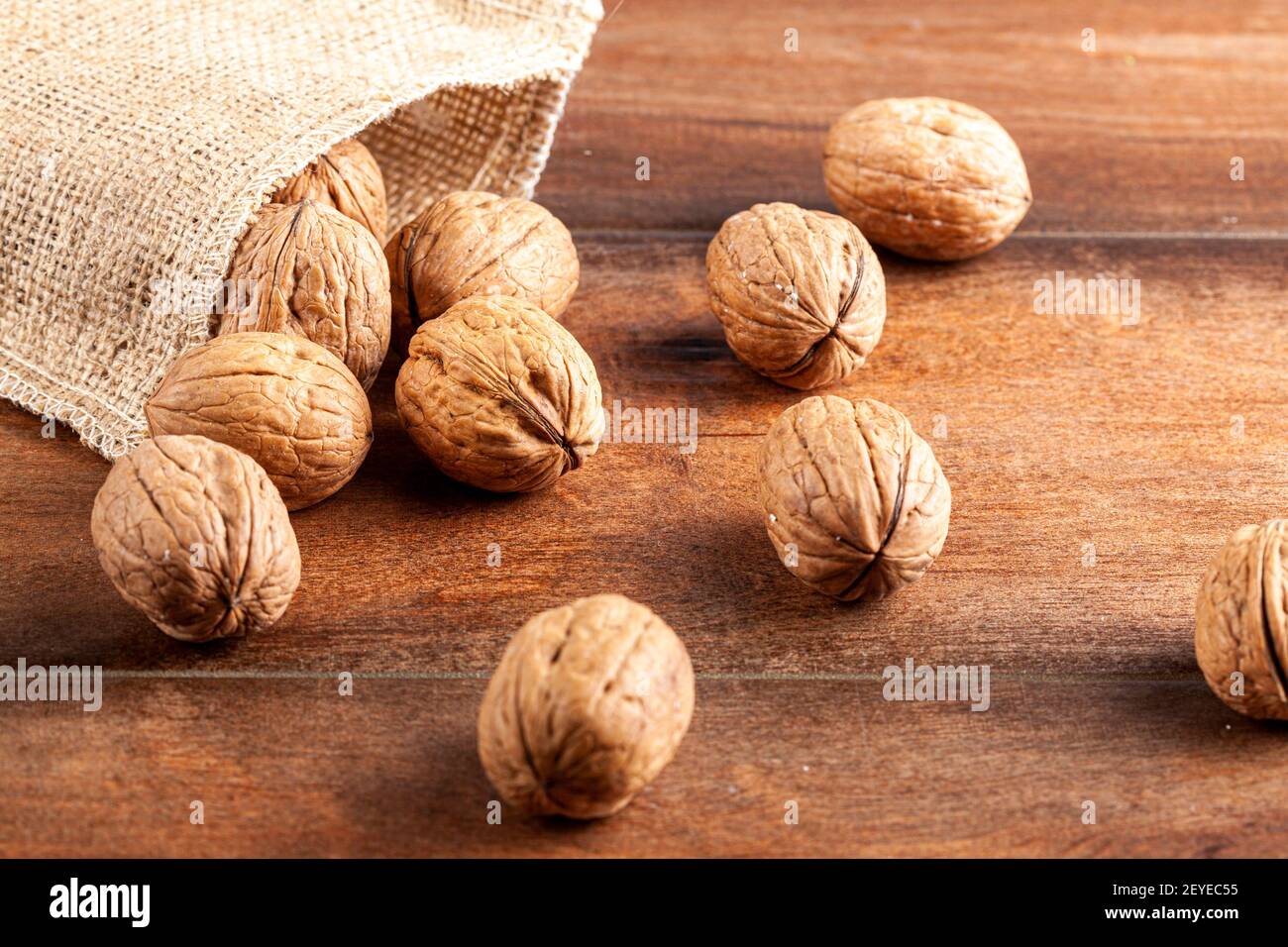 Un mucchio di noci inglesi fresche crude sparse su un tavolo di legno dalla borsa vintage burlop. Un'immagine rustica con un primo piano di messa a fuoco selettiva sulle noci i. Foto Stock