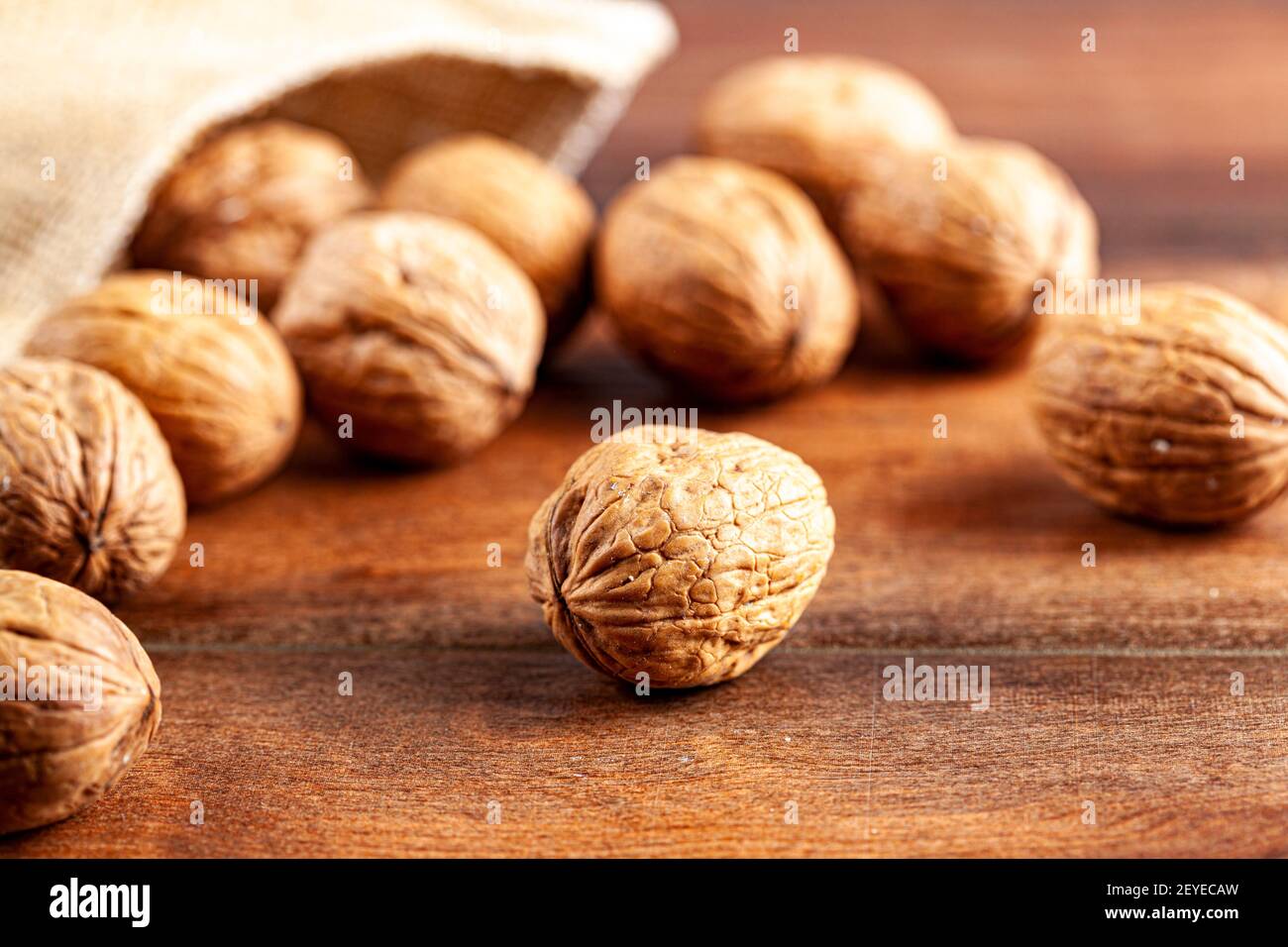Un mucchio di noci inglesi fresche crude sparse su un tavolo di legno dalla borsa vintage burlop. Un'immagine rustica con un primo piano di messa a fuoco selettiva sulle noci i. Foto Stock
