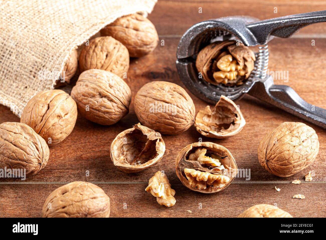 Immagine di messa a fuoco selettiva angolata delle noci in guscio sparse da un sacco vintage burlap su un tavolo di legno. Alcune sono incrinate con pinze in metallo noce Foto Stock