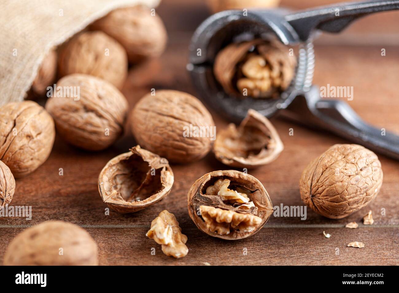 Immagine di messa a fuoco selettiva angolata delle noci in guscio sparse da un sacco vintage burlap su un tavolo di legno. Alcune sono incrinate con pinze in metallo noce Foto Stock