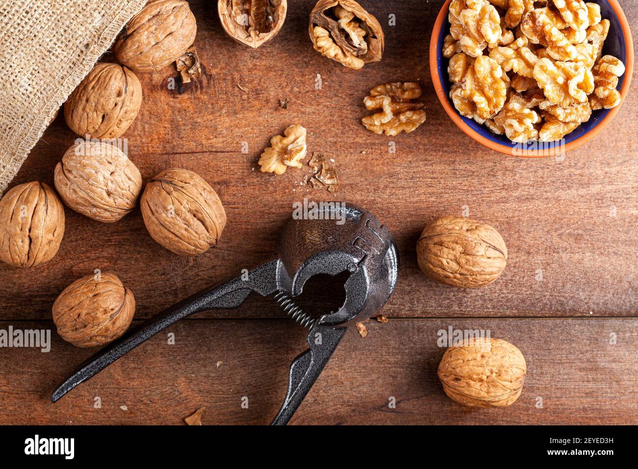 Immagine piatta raffigurante una pinza in ghisa per noci (un utensile per noci cracker) con noci fresche grezze in guscio su tavola di legno. Una piccola ciotola di nocciole Foto Stock