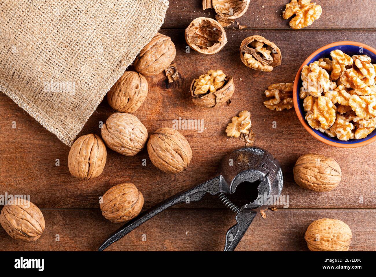 Immagine piatta raffigurante una pinza in ghisa per noci (un utensile per noci cracker) con noci fresche grezze in guscio su tavola di legno. Una piccola ciotola di nocciole Foto Stock