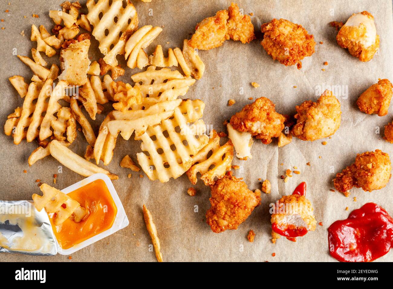 immagine piatta di un cibo disordinato con patatine fritte e bocconcini di pollo su carta da forno insieme al ketchup e altre salse e salse. Alcuni sono mangiati o Foto Stock