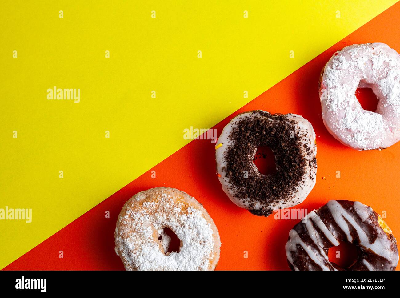 Assortimento di ciambelle dolci appena cotte decorative su due sfondo colorato. I deserti con diverse finiture e condimenti sono sul lato arancione whi Foto Stock