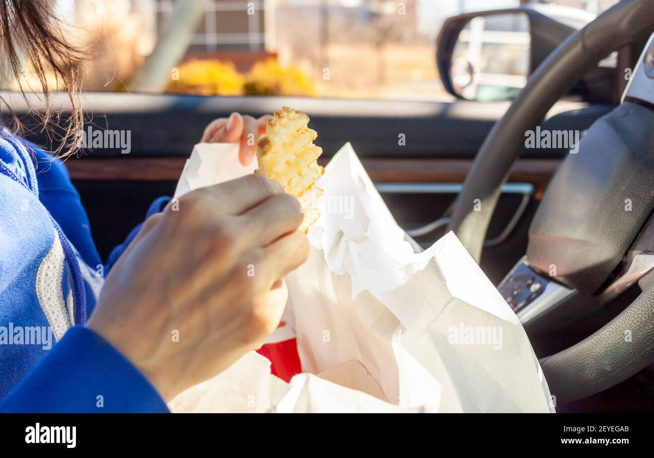 Una donna sta mangiando patatine fritte che ha ottenuto da un azionamento stradale attraverso la catena di fast food. Ha dei pacchi di cibo in grembo mentre mangia nel conducente Foto Stock