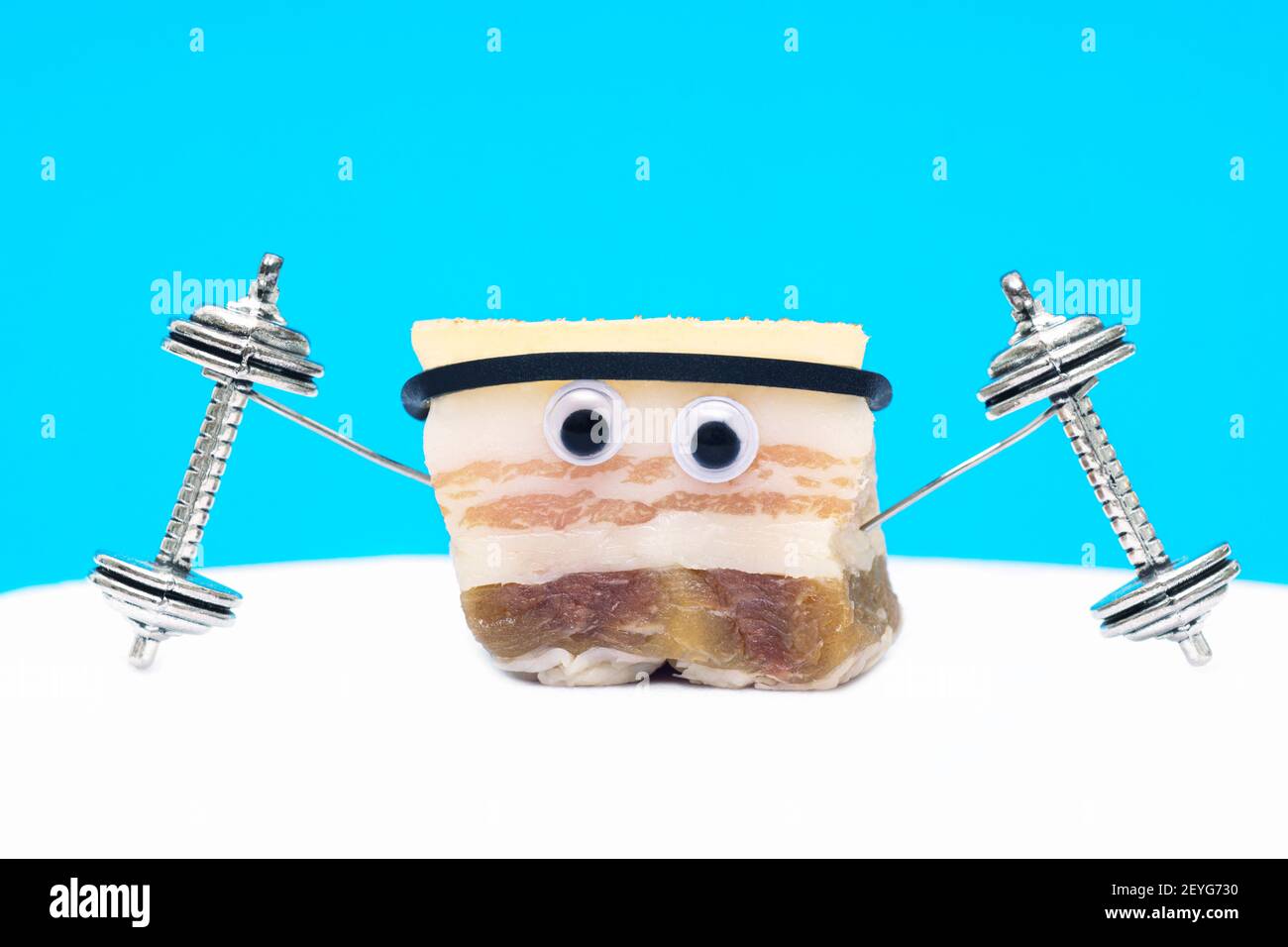 Primo piano di un personaggio divertente fatto di grasso di maiale salato sollevamento dumbbells su uno sfondo azzurro. Il concetto creativo di mantenersi in forma. Foto Stock