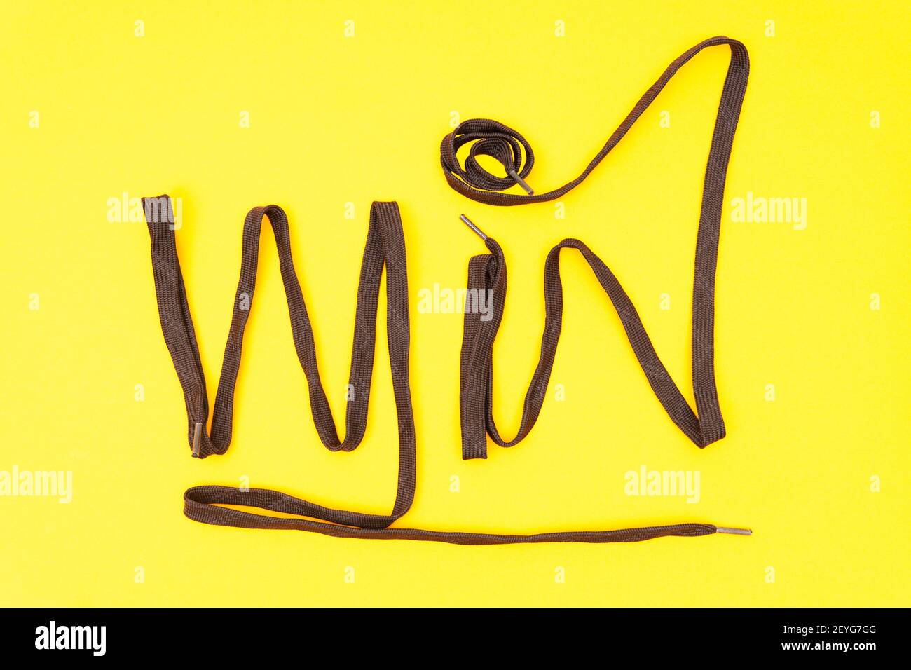 Word WIN fatto di scarpe atletiche marroni su sfondo giallo. Composizione creativa piatta. Foto Stock
