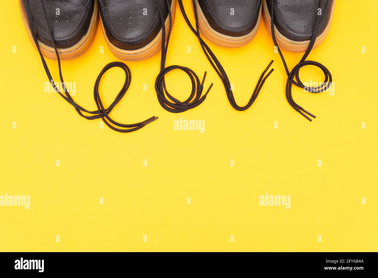 Ritagliare la vista di due paia di sneaker in pelle con la parola AMORE disposti delle scarpe su uno sfondo giallo. Condimento romantico come conce Foto Stock