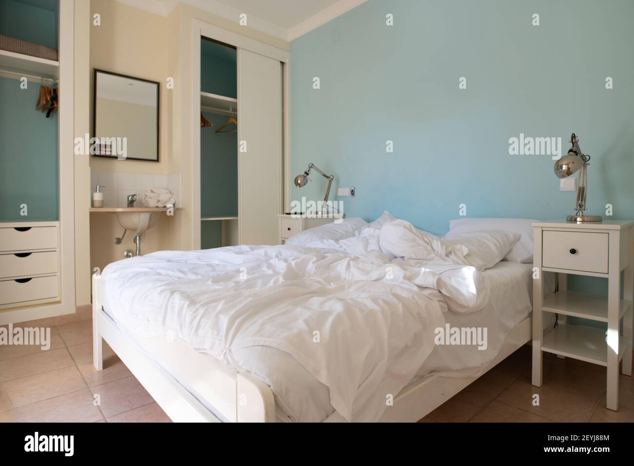 Camera da letto con letto non fatto con biancheria bianca e pareti blu Foto Stock