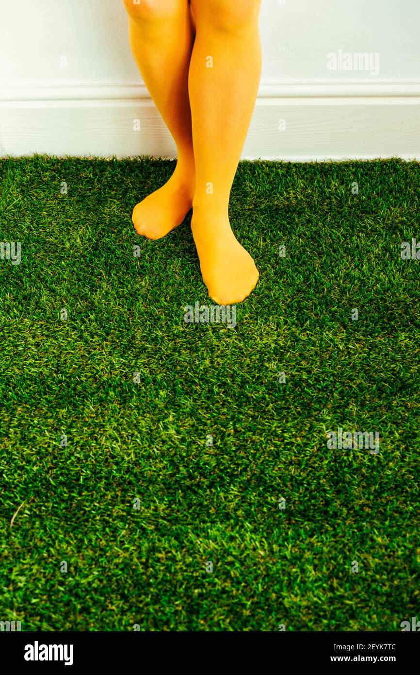 donna in abito giallo e collant in piedi su erba artificiale interno Foto Stock