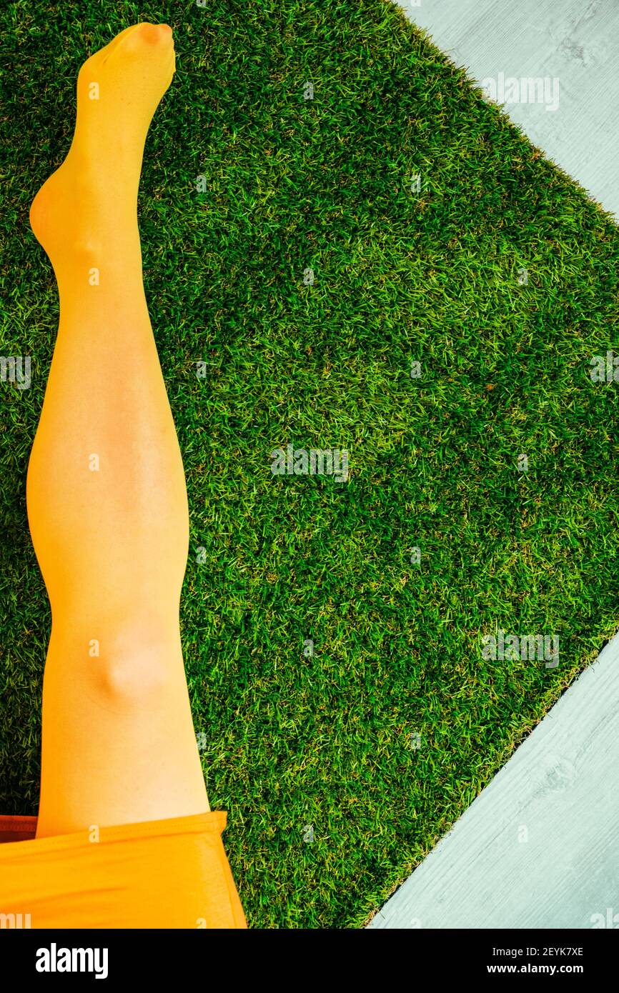 Donna in abito giallo e collant sdraiato su artificiale erba all'interno Foto Stock
