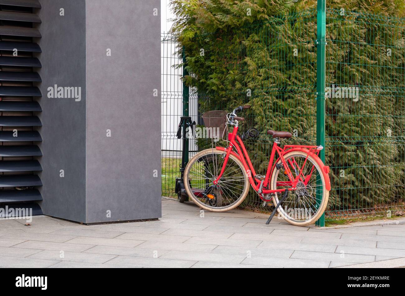 La bicicletta rossa si erge all'esterno di un edificio di uffici della città, fissato a una fasciatura cavo di sicurezza per biciclette Foto Stock