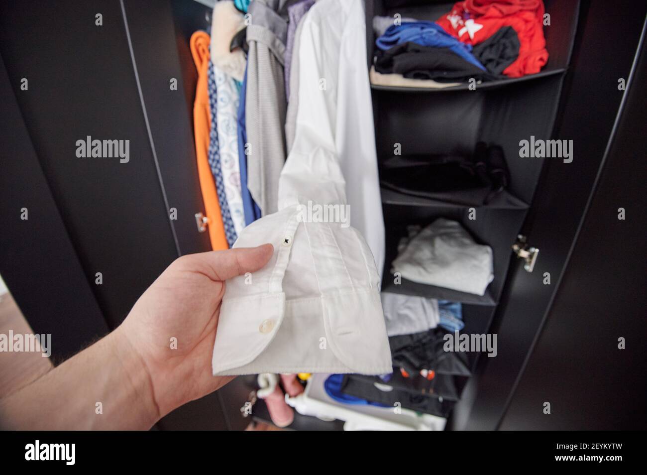 Uomo che ottiene camicia bianca dal guardaroba disordinato Foto Stock