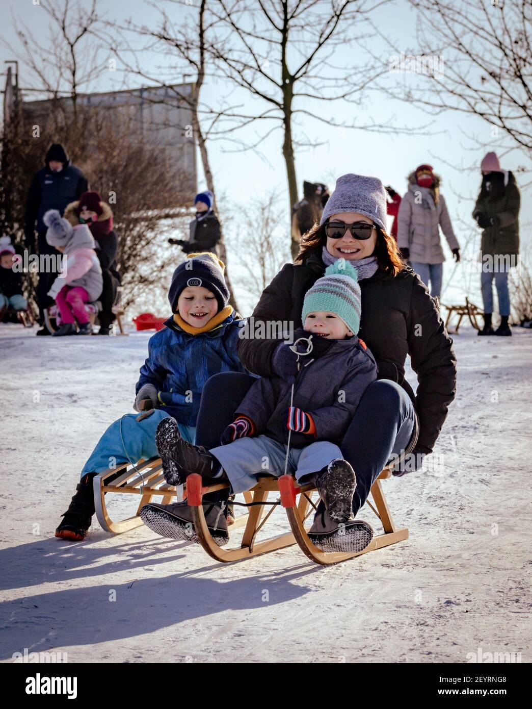 POZNAN, POLONIA - 17 gennaio 2021: Sorridente donna felice che si diverte con due bambini su scivoli di legno in un parco in una fredda giornata invernale Foto Stock