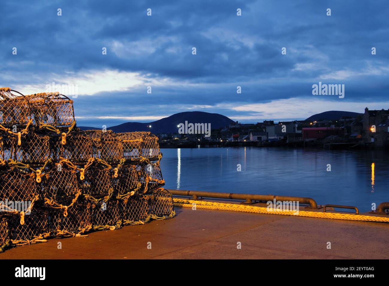 Gabbie di granchio e di aragosta nel porto scozzese con il blu nuvole case lontane e grande collina sullo sfondo Foto Stock