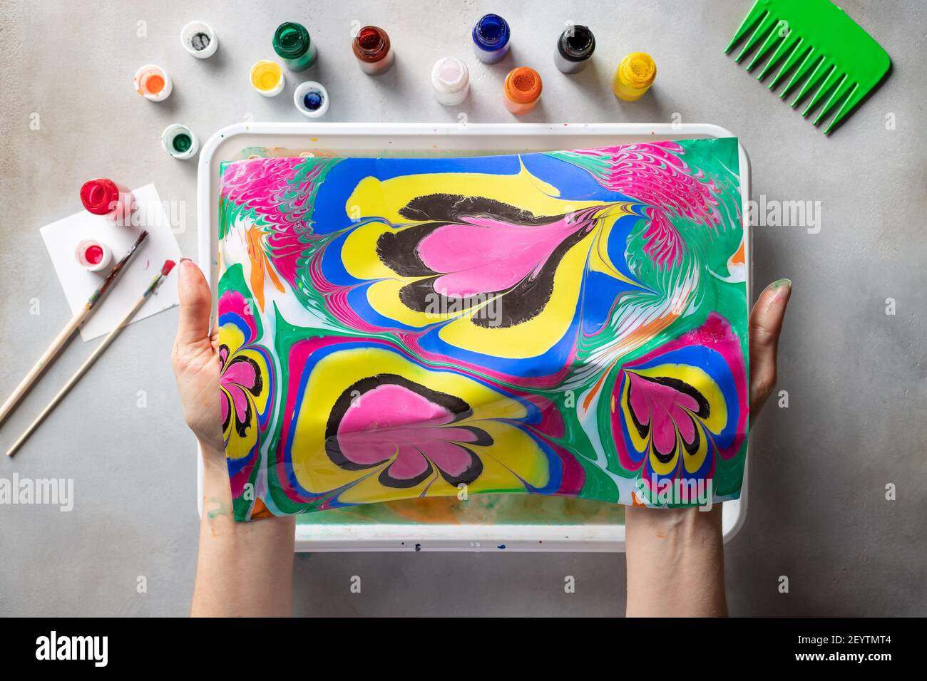 donna che tiene un disegno astratto, sopra il tavolo con pitture e attrezzi Foto Stock