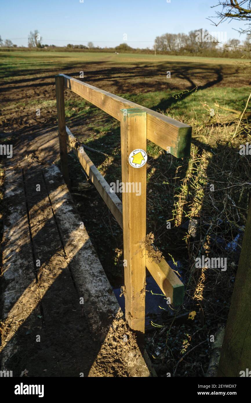 Una freccia gialla in una scheda circolare indica un percorso rurale pubblico su un piccolo ponte di legno, Oxfordshire, Regno Unito Foto Stock