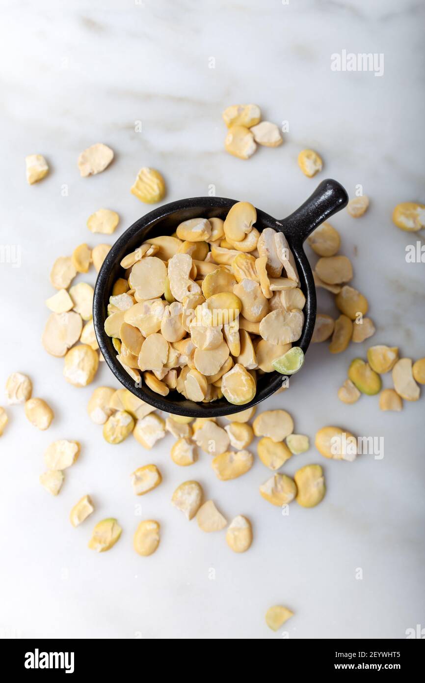 Fagioli secchi senza guscio in tazza nera su marmo bianco. Fagiolo Fava. Foto Stock