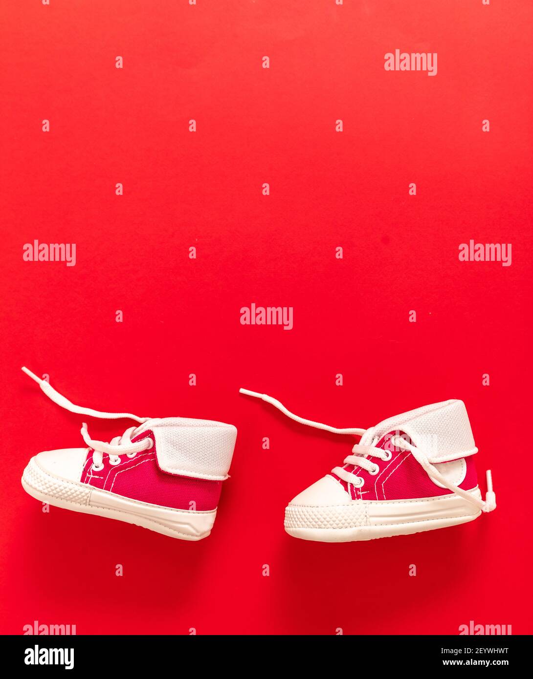 I primi passi per i bambini. Scarpe sportive per bambini che camminano su  sfondo di colore rosso. Scarpe da ginnastica per bambini di piccole  dimensioni, stivaletti in tela. Spazio, modello invito scheda