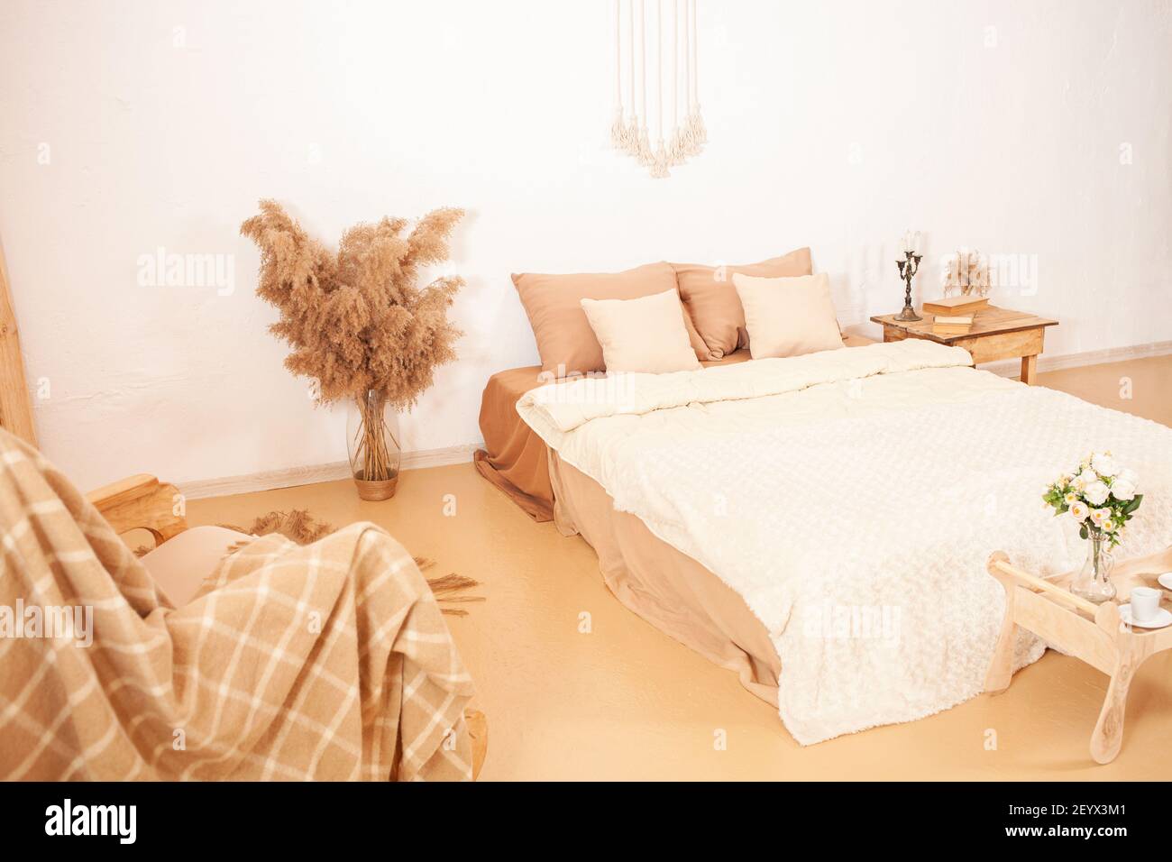 Interno beige marrone bianco. Camera da letto di tonalità chiare. Una sedia  basculante con una plaid, uno specchio in una cornice di legno, fiori  pampas pianta. Decorazioni per t Foto stock 