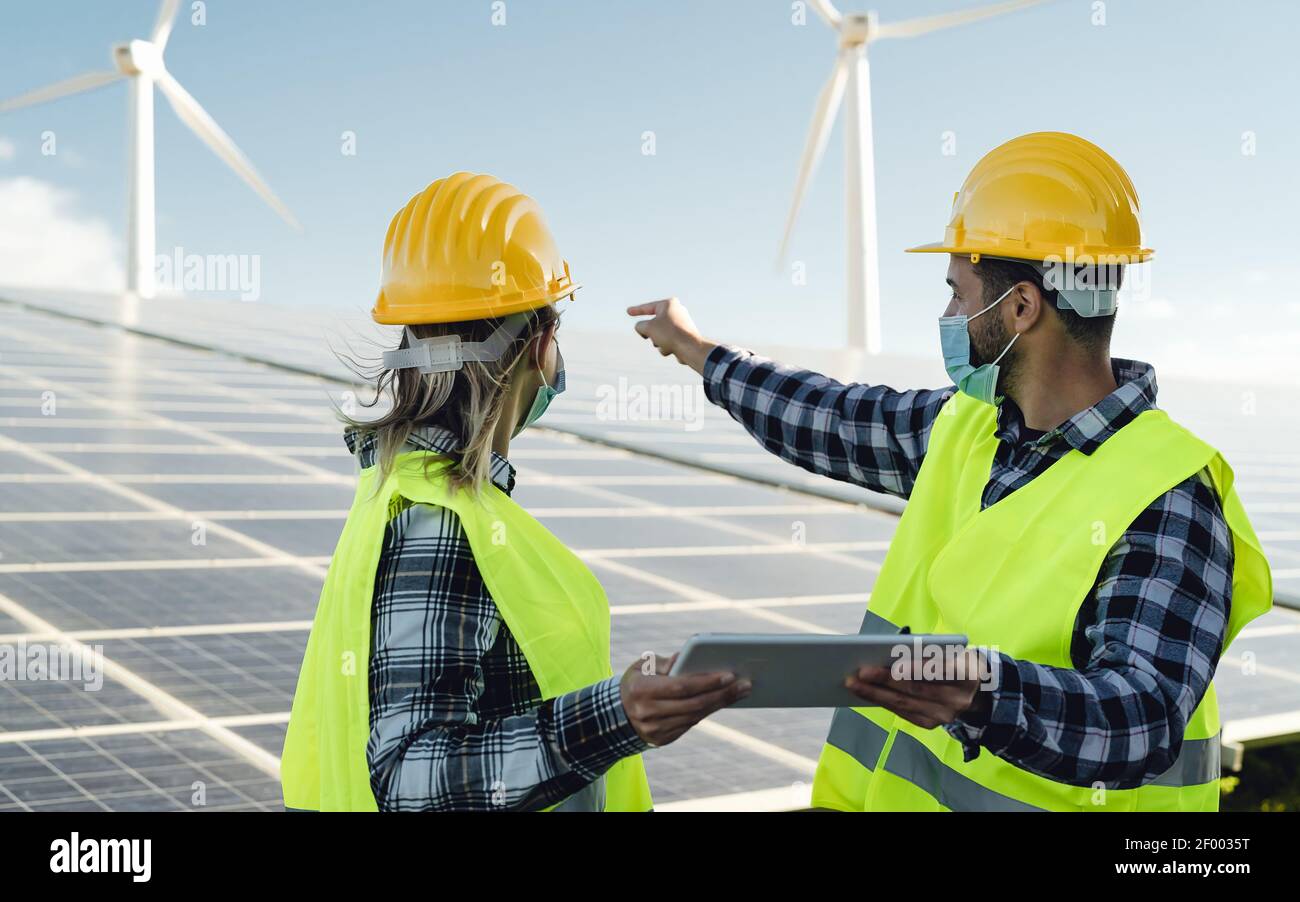 Persone che lavorano per l'energia alternativa con turbine eoliche e solari pannello mentre si indossa la maschera facciale durante l'epidemia di virus corona Foto Stock Persone che lavorano per l'energia alternativa con turbine eoliche e solari pannello mentre si indossa la maschera facciale durante l'epidemia di virus corona Foto Stock