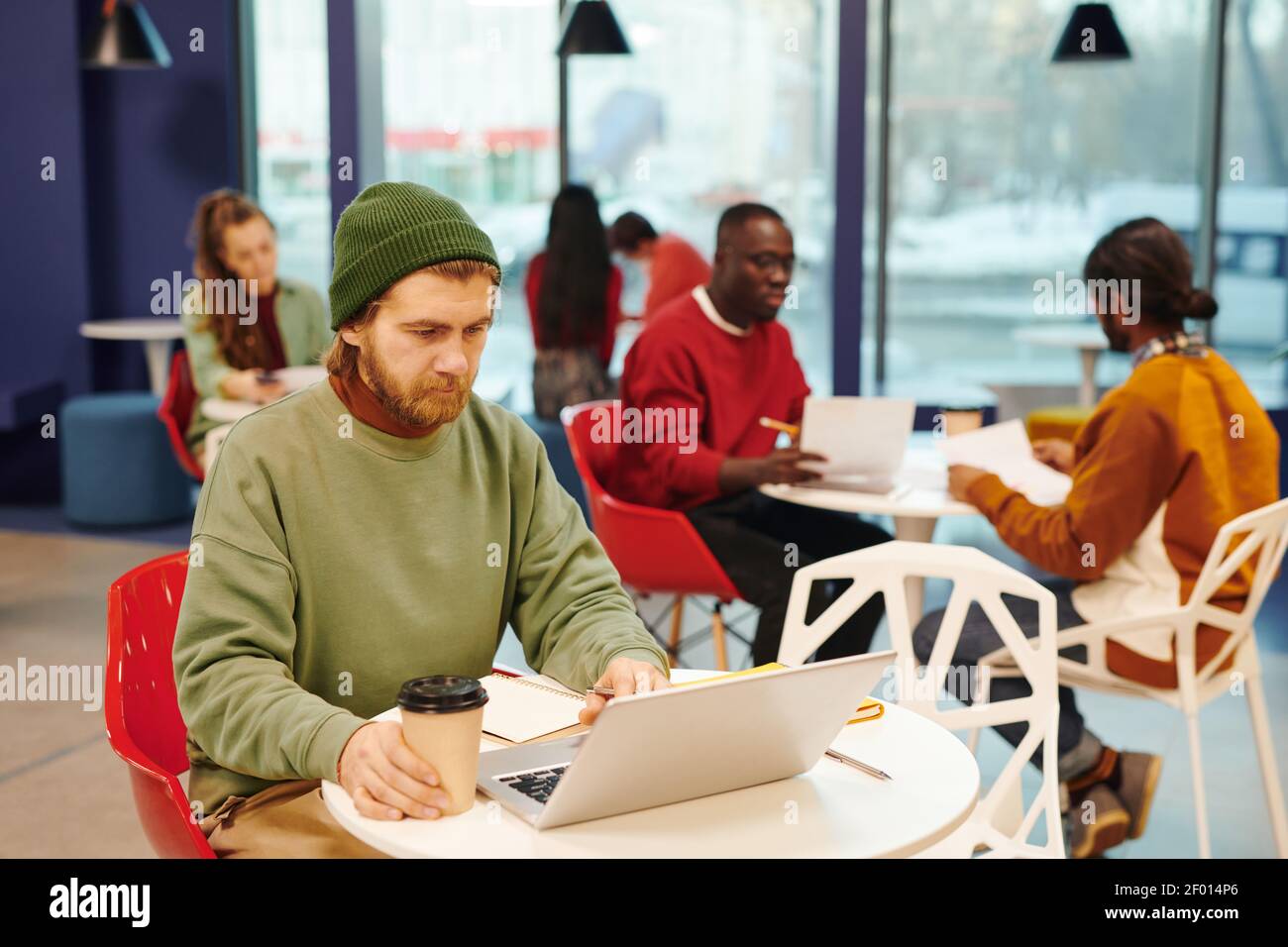 Donna d'affari con un bicchiere di caffè che guarda il computer portatile display mentre si è seduti alla scrivania in ufficio open space contro i suoi colleghi Foto Stock