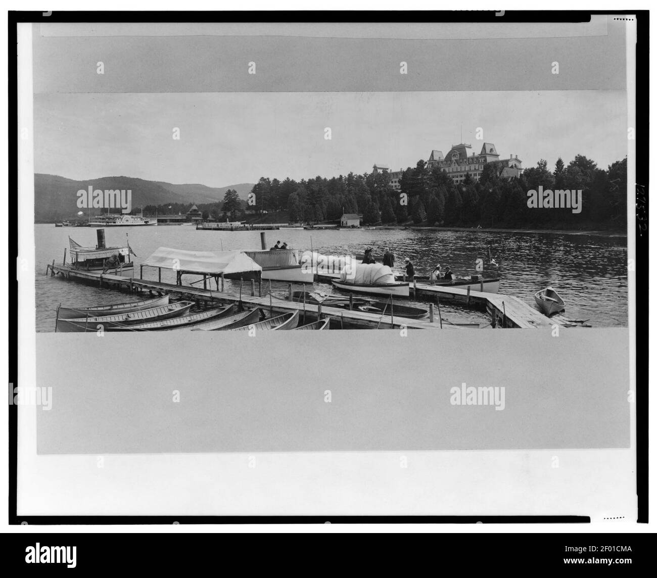 Piers, barche e persone in primo piano con il Fort William Henry Hotel in background, Lake George, New York Foto Stock