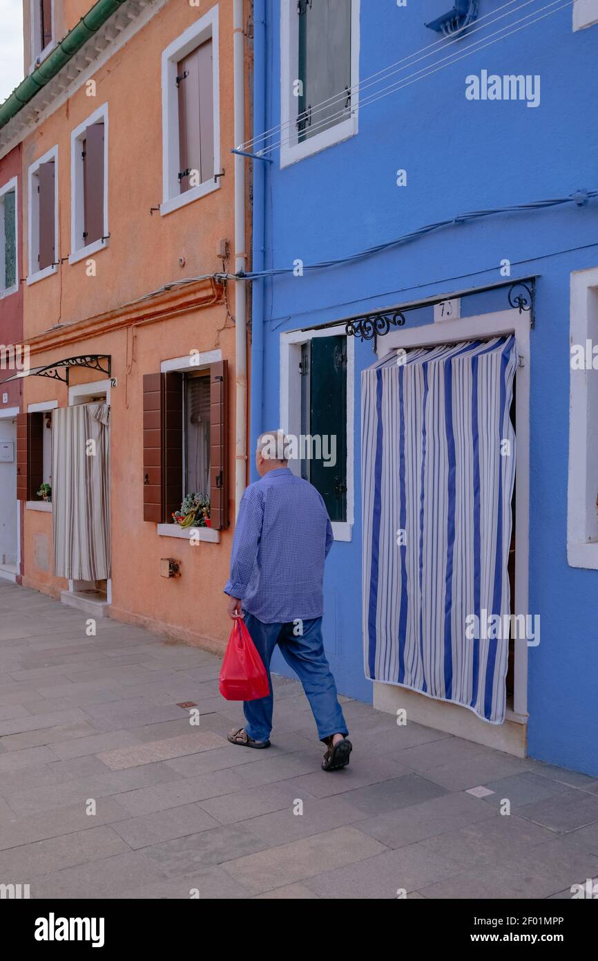 Un uomo cammina lungo il canale con luminose case veneziane colorate sull'isola di Burano - Venezia, Veneto, Italia - Scenic and Postcard Perfect Beautiful View Foto Stock