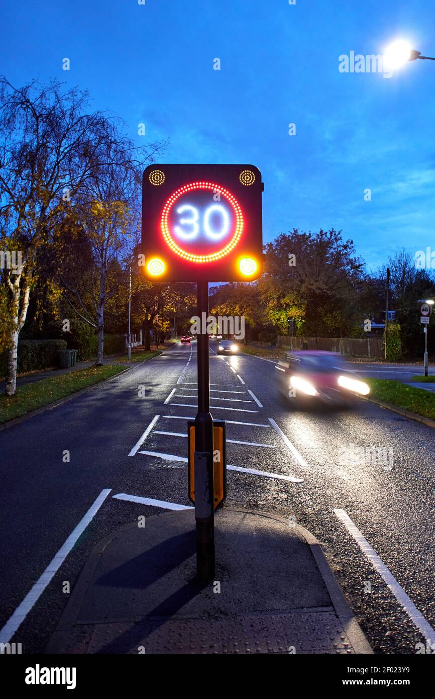 Strada a 2 vie che mostra traffico in avvicinamento e in transito di notte con un segnale LED elettronico del limite di velocità di 30 miglia all'ora (mph). Foto Stock