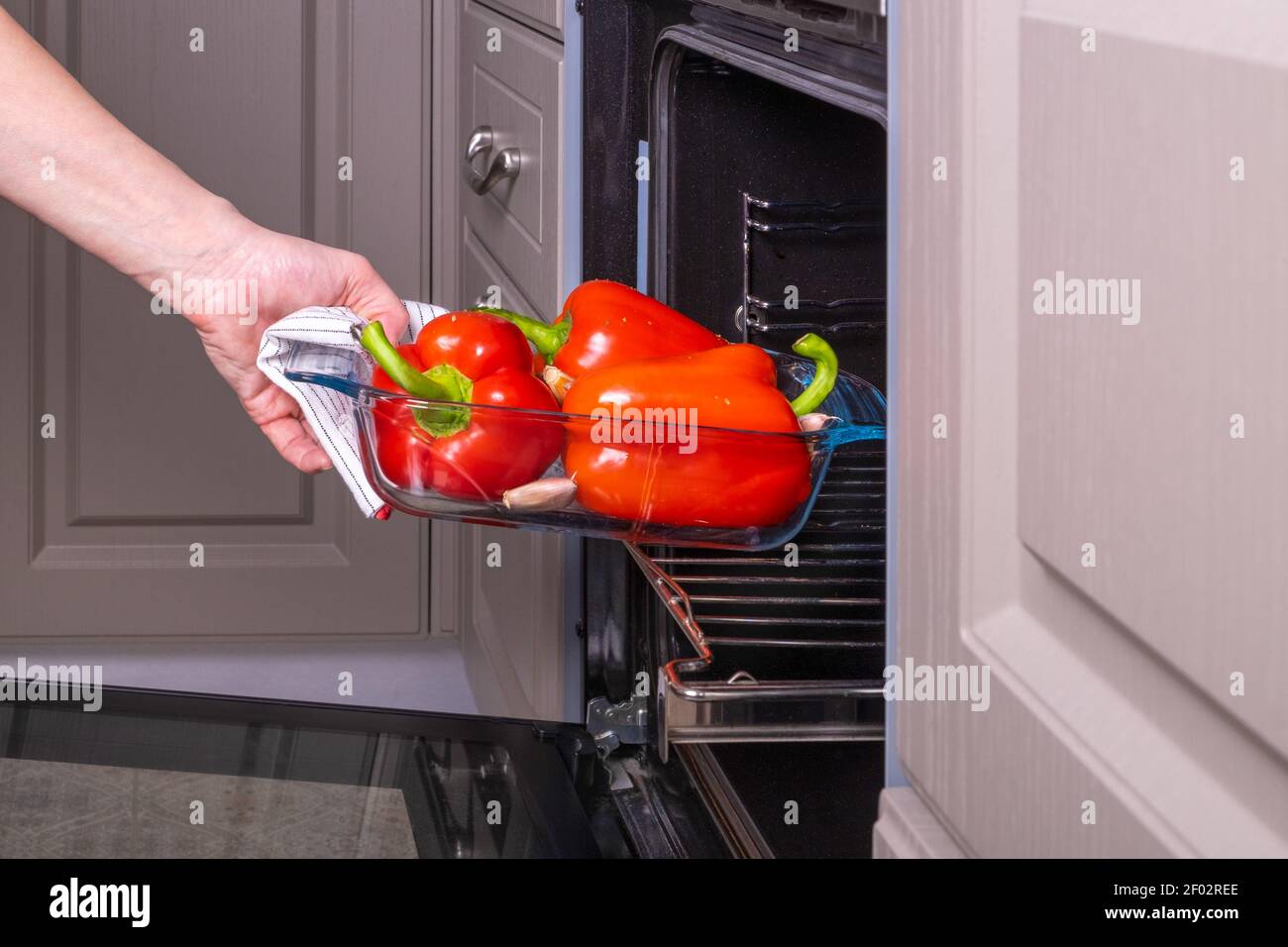 Donna casalinga mette una vaschetta di vetro ignifuga di peperoni rossi maturi per la cottura in un forno elettrico. Foto Stock