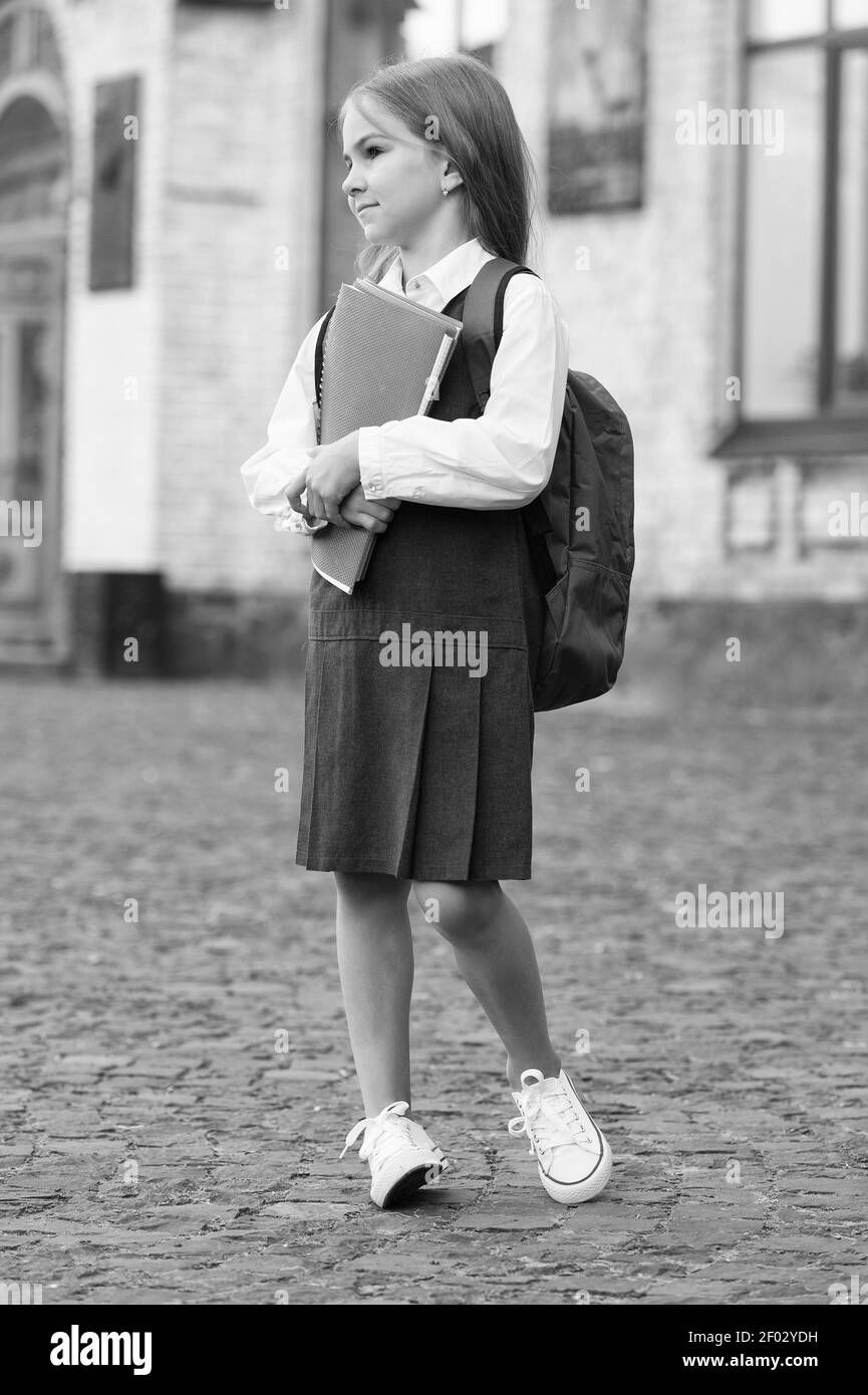Piccolo capretto in uniforme formale con sguardo di ritorno alla scuola trasporta la borsa che tiene i libri e le forniture, università. Foto Stock