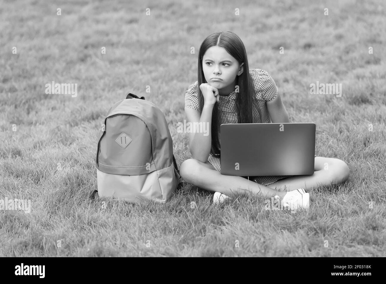 triste ragazza teen utilizzando notebook per l'istruzione online e l'apprendimento seduto in parco su erba verde con zaino, di nuovo a scuola. Foto Stock