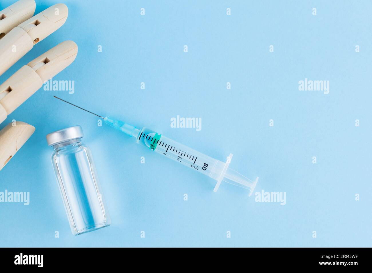 Vaccino, siringa e mano umana di legno. Fiala medica e siringa su sfondo blu. Concetto di assistenza sanitaria e prevenzione delle malattie. Vista dall'alto Foto Stock
