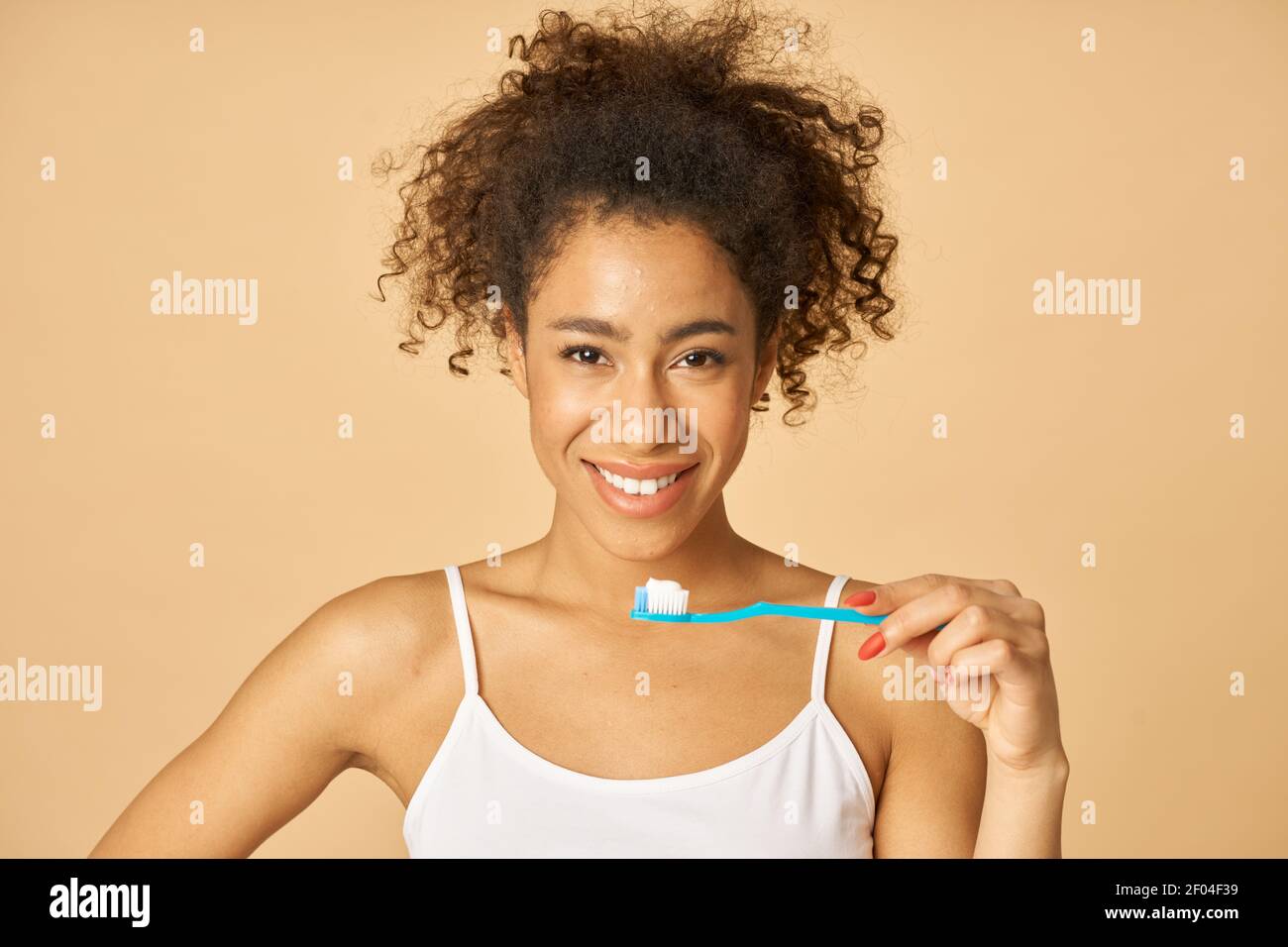 Ritratto di carina giovane razza mista donna spazzolando i denti al mattino, in posa isolata su sfondo beige. Concetto di assistenza sanitaria dentale Foto Stock