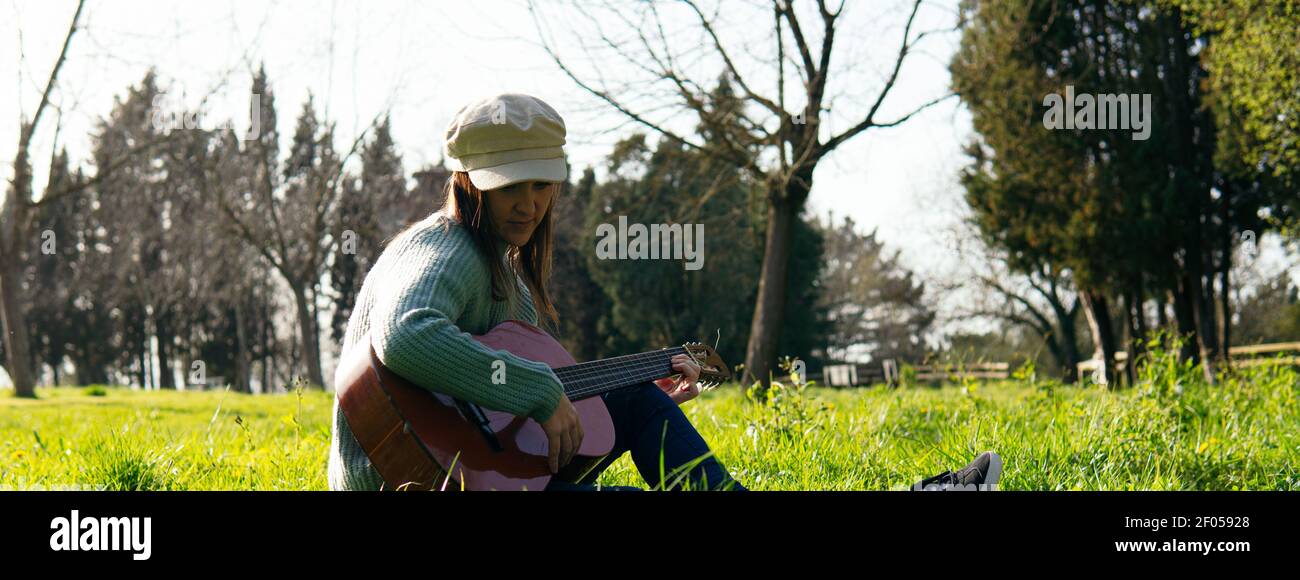 bella donna in cappello che suona la chitarra spagnola in un parco al crepuscolo in primavera Foto Stock