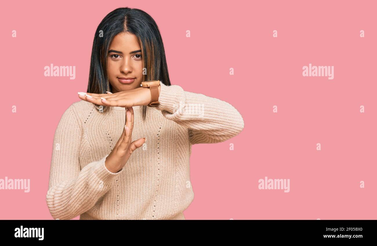 Giovane ragazza latina che indossa maglia invernale in lana facendo il gesto del tempo con le mani, il viso frustrato e serio Foto Stock