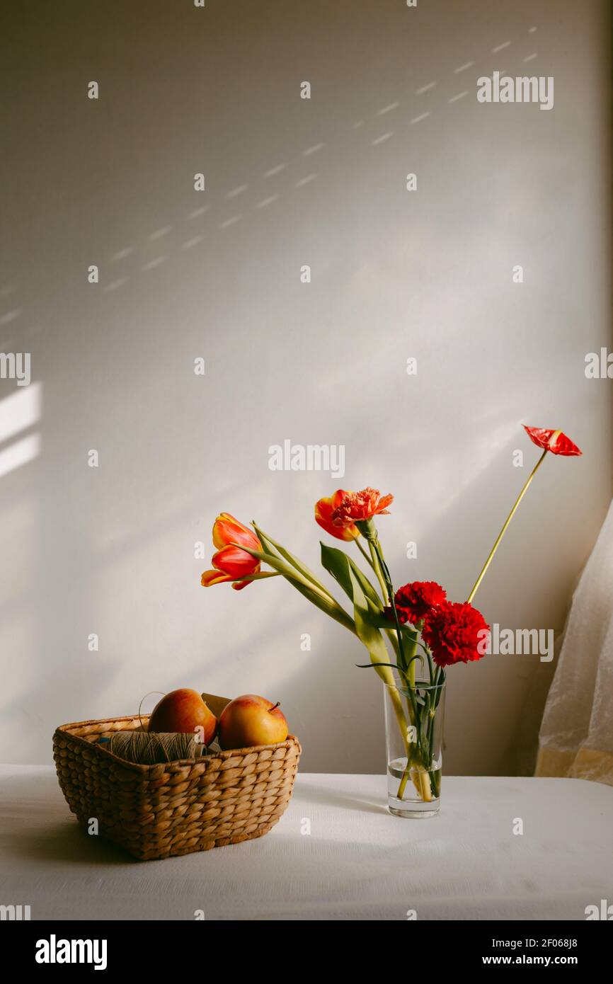 Vaso con tulipani in fiore e garofano posto sul tavolo vicino mele in recipiente di vimini Foto Stock