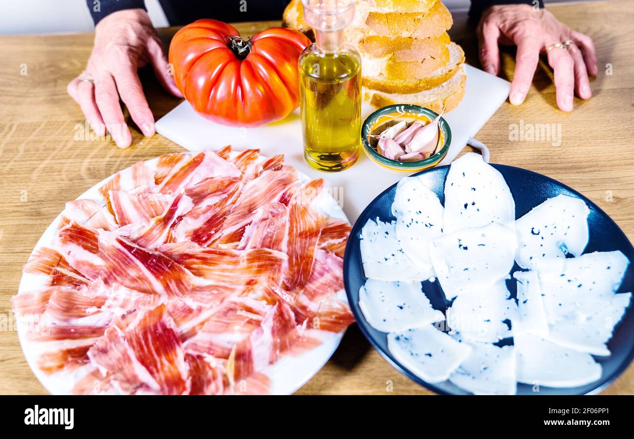 Anonimo persona che cucina un tipico catalano o cibo spagnolo. Pane con pomodoro, prosciutto iberico, formaggio di capra, olio d'oliva e aglio. Cibo tradizionale Foto Stock