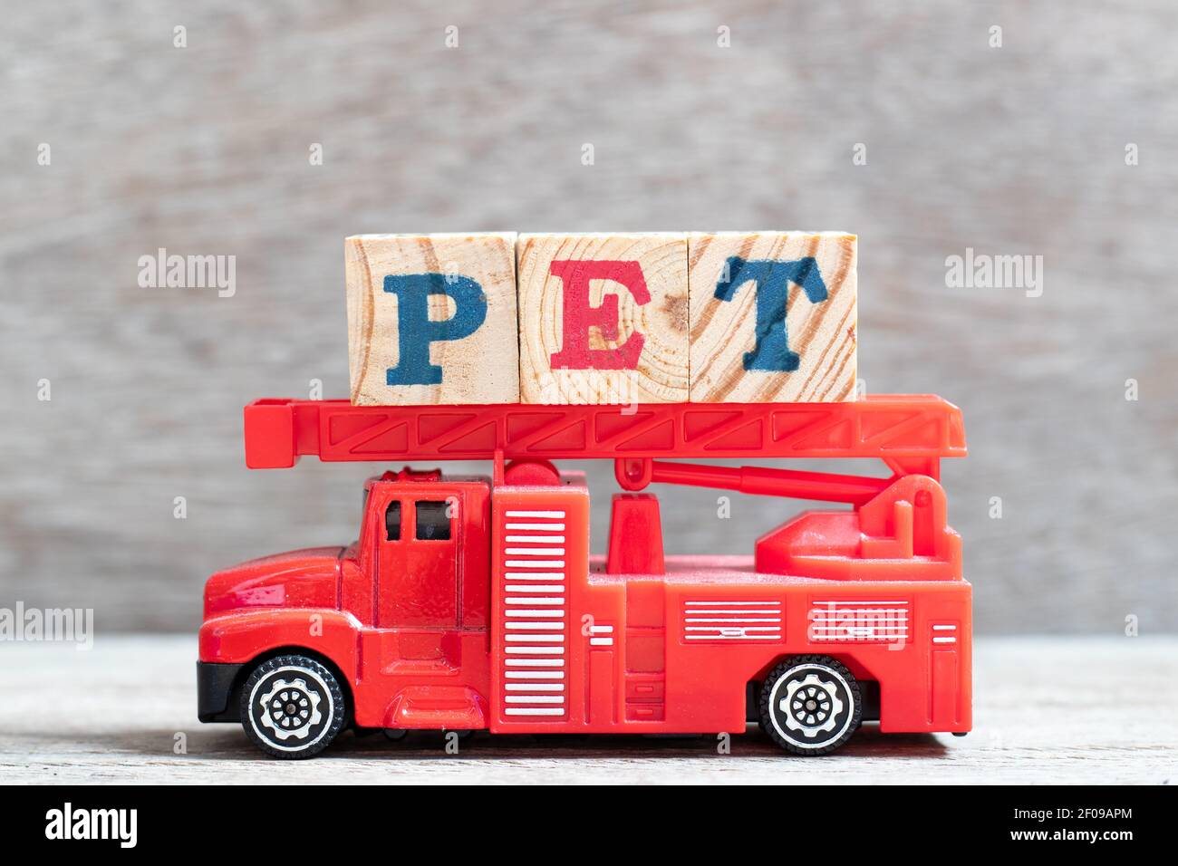 Il camion antincendio rosso tiene il blocco di lettere nella parola PET (animale o abbreviazione di polietilentereftalato) su fondo di legno Foto Stock