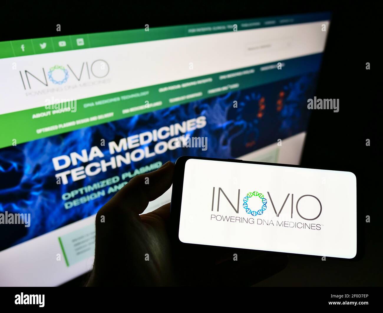 Persona che detiene smartphone con logo della società di biotecnologia statunitense Inovio Pharmaceuticals Inc. Sullo schermo davanti al sito web. Mettere a fuoco il display del telefono. Foto Stock