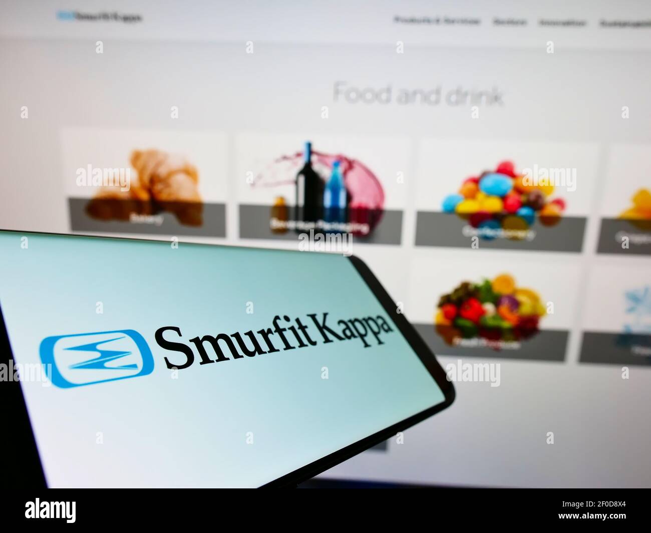 Telefono cellulare con logo aziendale della società irlandese di confezionamento Smurfit Kappa Group plc sullo schermo davanti alla pagina web. Mettere a fuoco il centro del display del telefono. Foto Stock