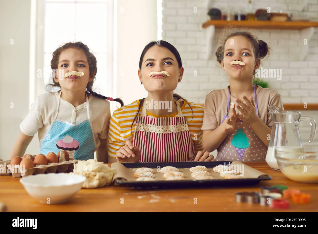 I bambini piccoli e la madre giovane giocano con l'impasto mentre fanno biscotti a casa Foto Stock