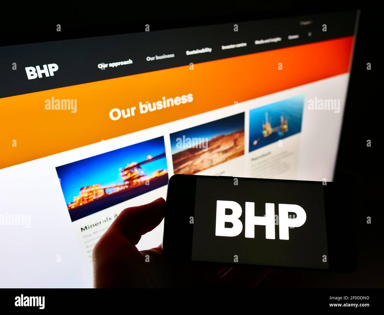 Persona che detiene il telefono cellulare con il logo aziendale della società mineraria BHP Group sullo schermo davanti alla pagina Web. Focus sul display del cellulare. Foto Stock