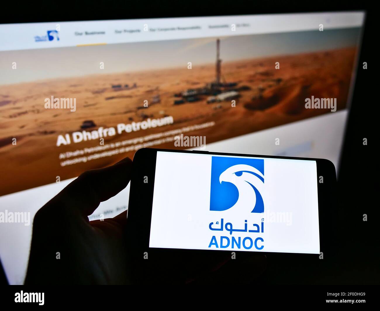 Persona che detiene il cellulare con il logo della Abu Dhabi National Oil Company (ADNOC, petrolio e gas) sullo schermo davanti alla pagina web. Mettere a fuoco il display del telefono. Foto Stock