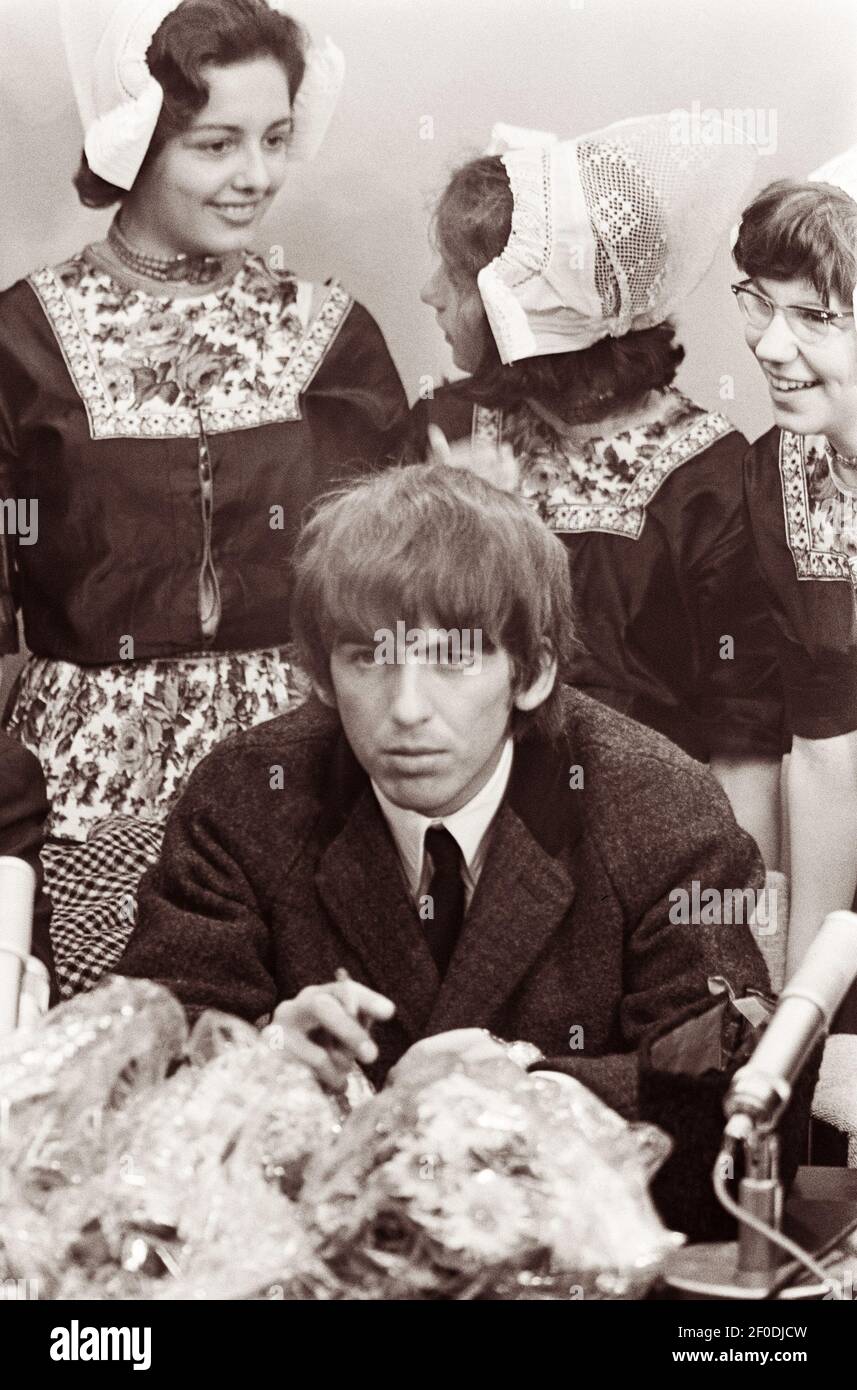 Le ragazze olandesi si levano in piedi dietro il chitarrista principale George Harrison ad una conferenza stampa dell'aeroporto di Schiphol quando i Beatles sono arrivati ad Amsterdam, Olanda il 5 giugno 1964. Foto Stock