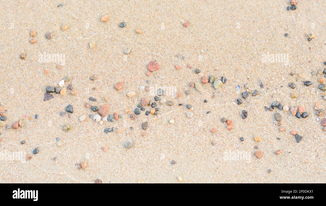 Piccole pietre di ciottoli sulla spiaggia di sabbia bagnata. Ampio formato, panoramica. Messa a fuoco selettiva, spazio di copia. Foto Stock