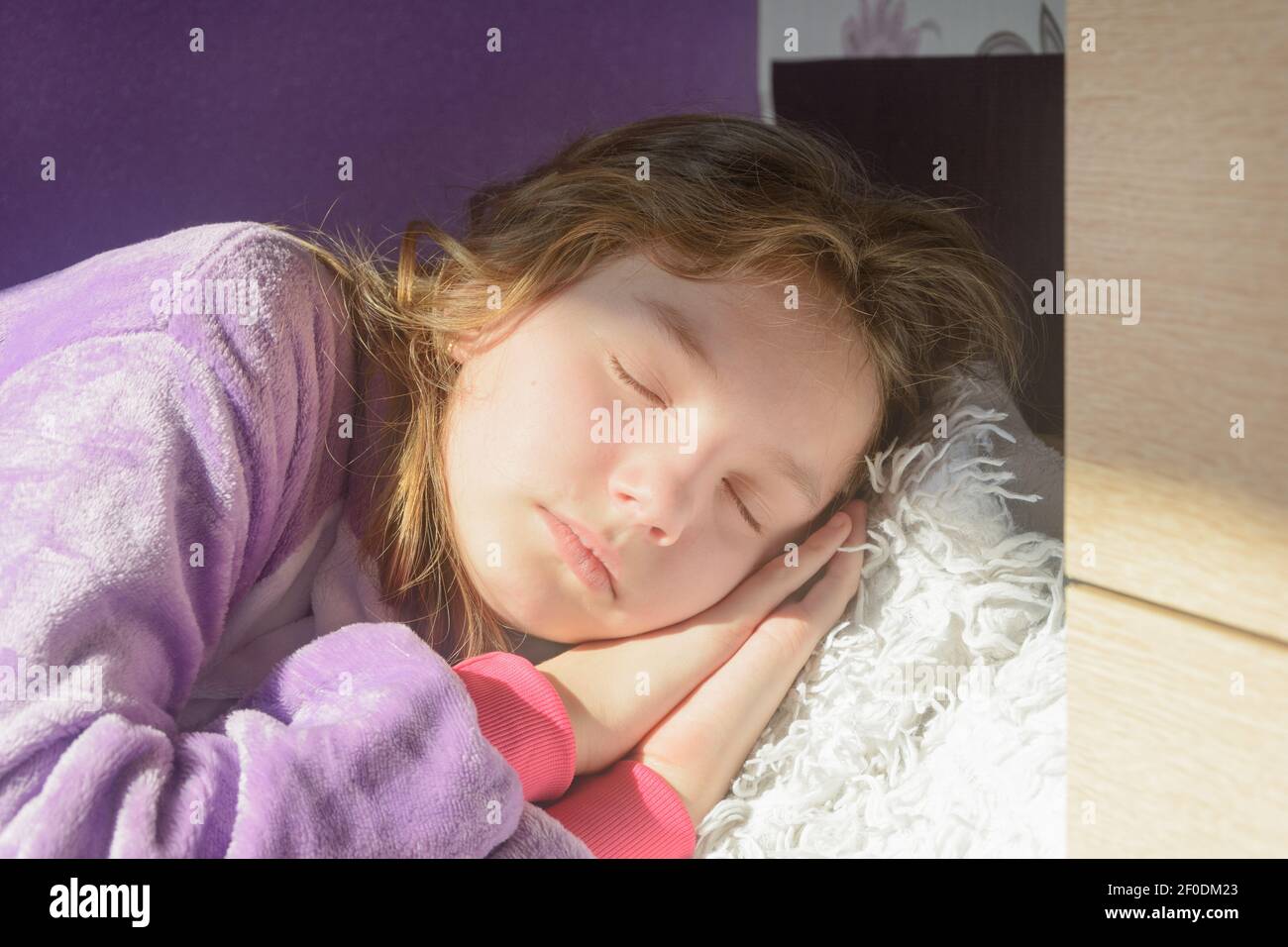 La ragazza adolescente dorme a casa con le braccia sotto la testa. Raggi sole sulla faccia della signora. Mattina dormire. Primo piano, messa a fuoco selettiva. Foto Stock